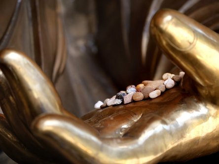 Offene, goldene Hand einer Buddha-Statue, die kleine Steinchen haelt