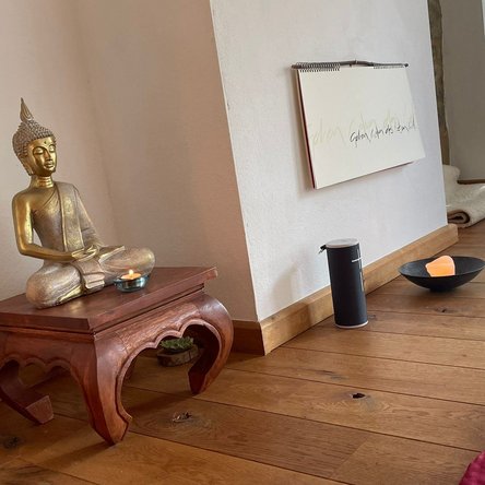 Goldene Buddha-Figur auf Holzhocker, Kerze, Kaligrafie, Holzboden